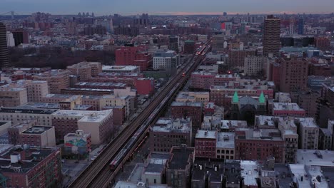 La-Toma-Aérea-Sigue-A-Los-Trenes-De-Cercanías-Elevados-Que-Atraviesan-La-Ciudad-De-Harlem,-Nueva-York,-Justo-Después-Del-Amanecer