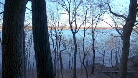 a horizontal pan from a higher vantage point of a river as seen through forest trees during a bright and sunny cloudless afternoon