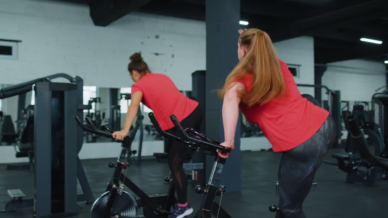 건강한 백인 여성 그룹이 체육관에서 정지 자전거 기계 자전거에서 운동을합니다.