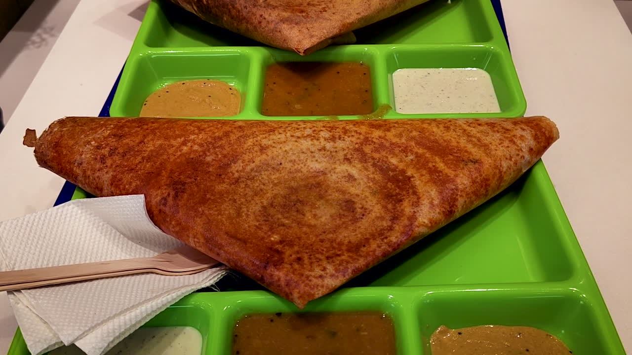 Indisk Mysore dosa servert med sambar og kokosnøtt-chutney på et brett på restaurant.