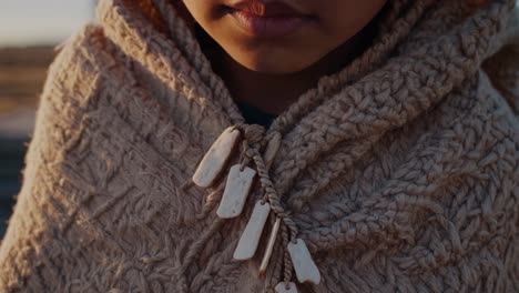 close up of a young child wearing a handmade poncho adorned with bone ornaments, possibly signifying cultural heritage or spiritual beliefs, during a serene sunset