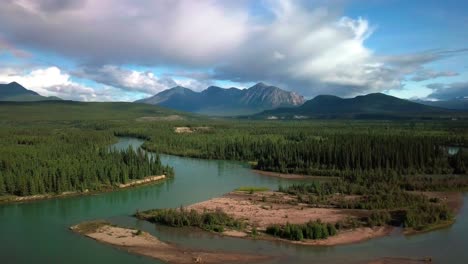 espectacular vuelo panorámico en el campo sobre el río verde yukon takhini por un bosque de árboles de hoja perenne y la cordillera del monte ingram en el fondo en un espectacular día azul soleado, canadá, antena aérea
