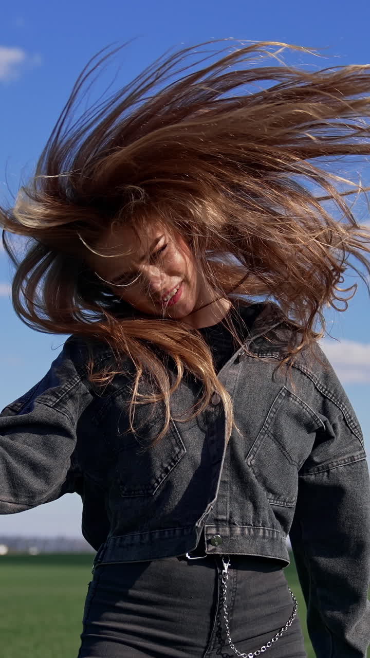 Pop female singer near the microphone outdoors. Pretty girl in denim suit twirling her head with long hair while singing on green field background. Vertical video