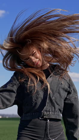 pop female singer near the microphone outdoors. pretty girl in denim suit twirling her head with long hair while singing on green field background. vertical video