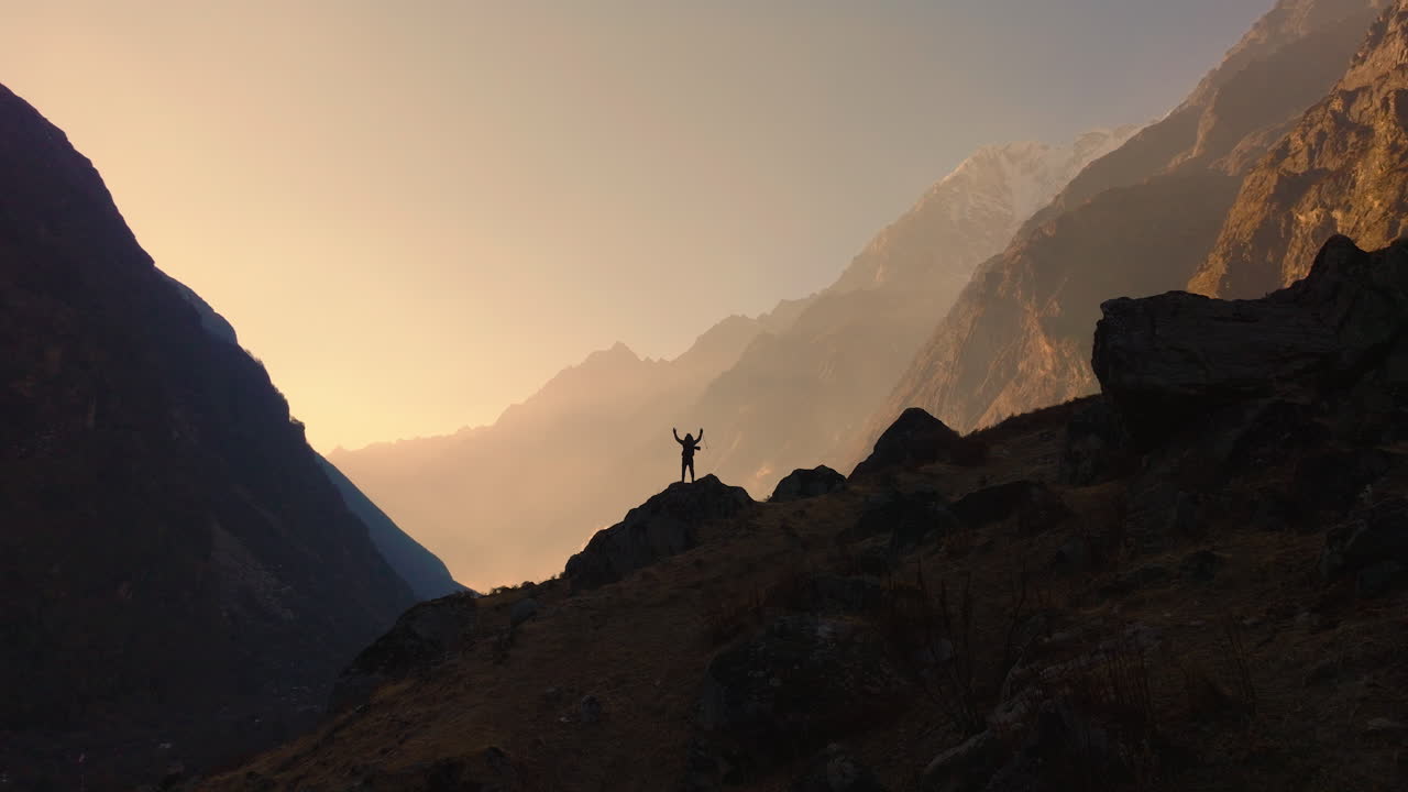 A wide drone shot captures the silhouette of a male tourist entering the majestic, snow-capped Himalayan landscape of Langtang National Park, Nepal, during the mesmerizing sunset golden hour.