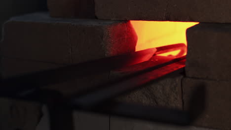 blacksmith turns a red hot metal hook in a furnace oven in a workshop