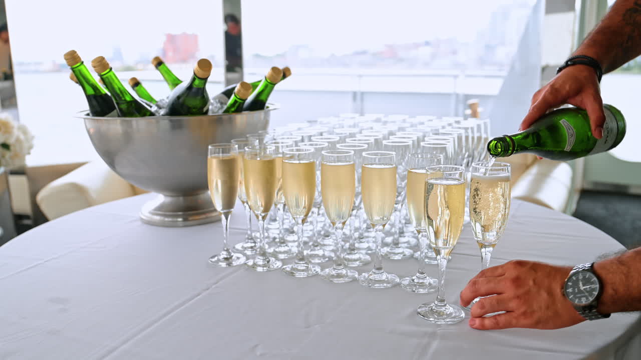 Mannlige hender heller champagne i høye glass som står på bordet dekket med hvit duk. Restaurant om bord på cruise-elvebåten. Nærbilde