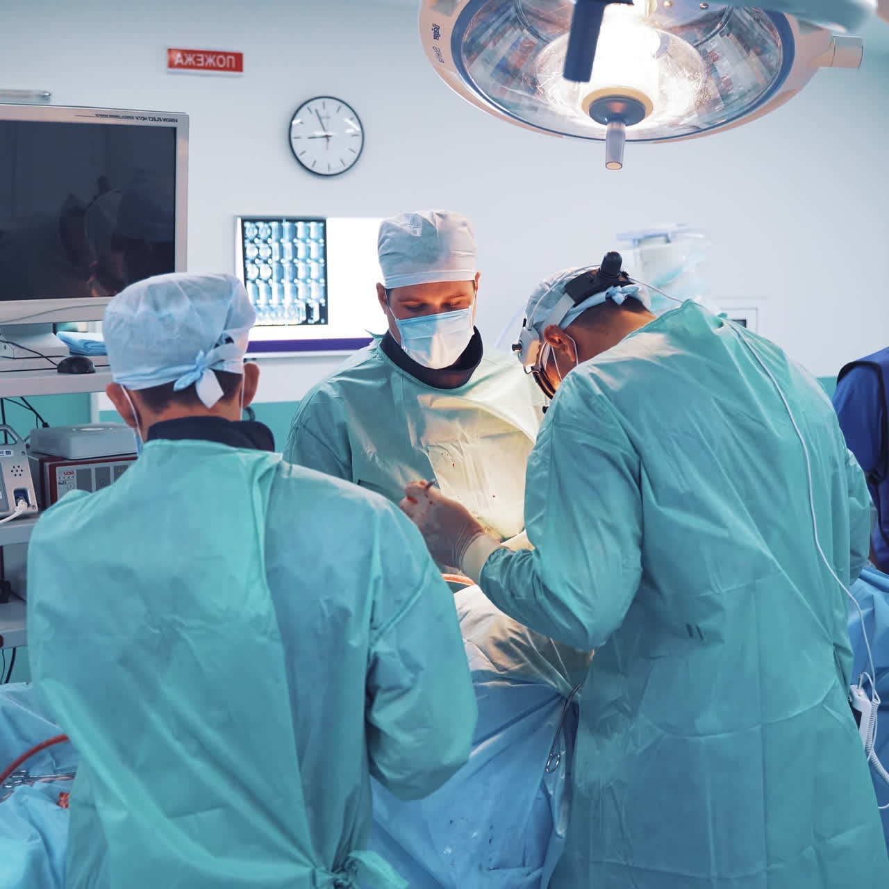 Several doctors treat the patient in contemporary operating room. Three professional surgeons with assistants perform an operation in modern medical center.
