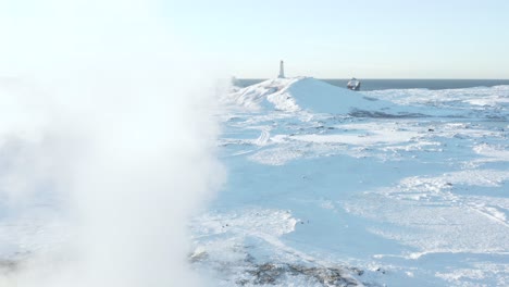 Volando-Más-Allá-Del-Vapor-Del-Géiser-Gunnuhver-Hacia-El-Icónico-Faro-De-Reykjanes