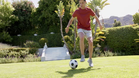 Fokussierter-Biracial-Mann,-Der-Fußballfähigkeiten-Im-Sonnigen-Garten-übt,-Kopierraum,-Zeitlupe