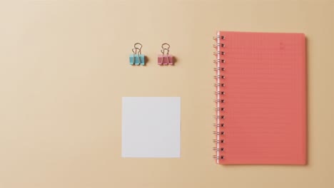 Overhead-view-of-red-notebook-and-school-stationery-arranged-on-beige-background,-in-slow-motion