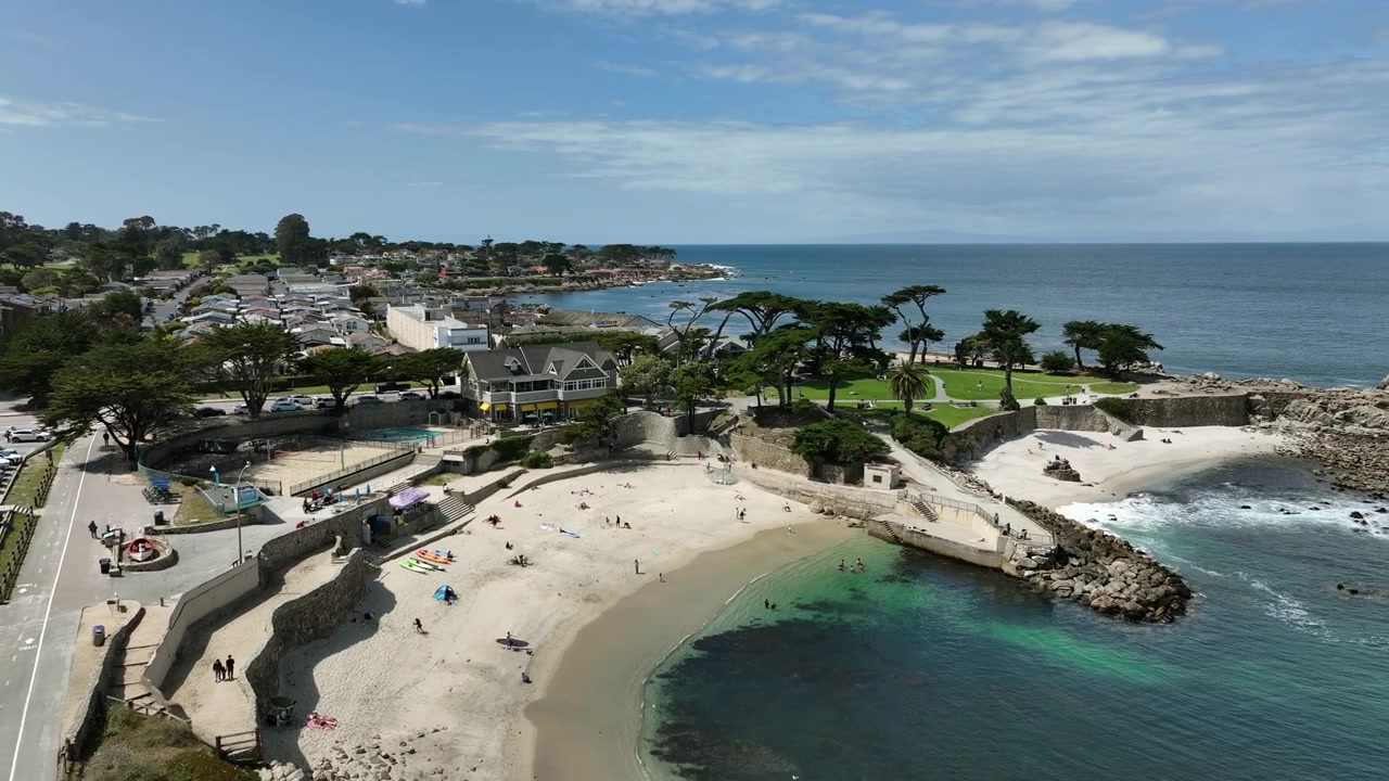 Riprese aeree cinematografiche con drone di Lovers Point Park a Pacific Grove, CA, che mostrano spiagge sabbiose, costa rocciosa, acqua turchese dell'Oceano Pacifico, strade costiere, case fronte mare, Baia di Monterey