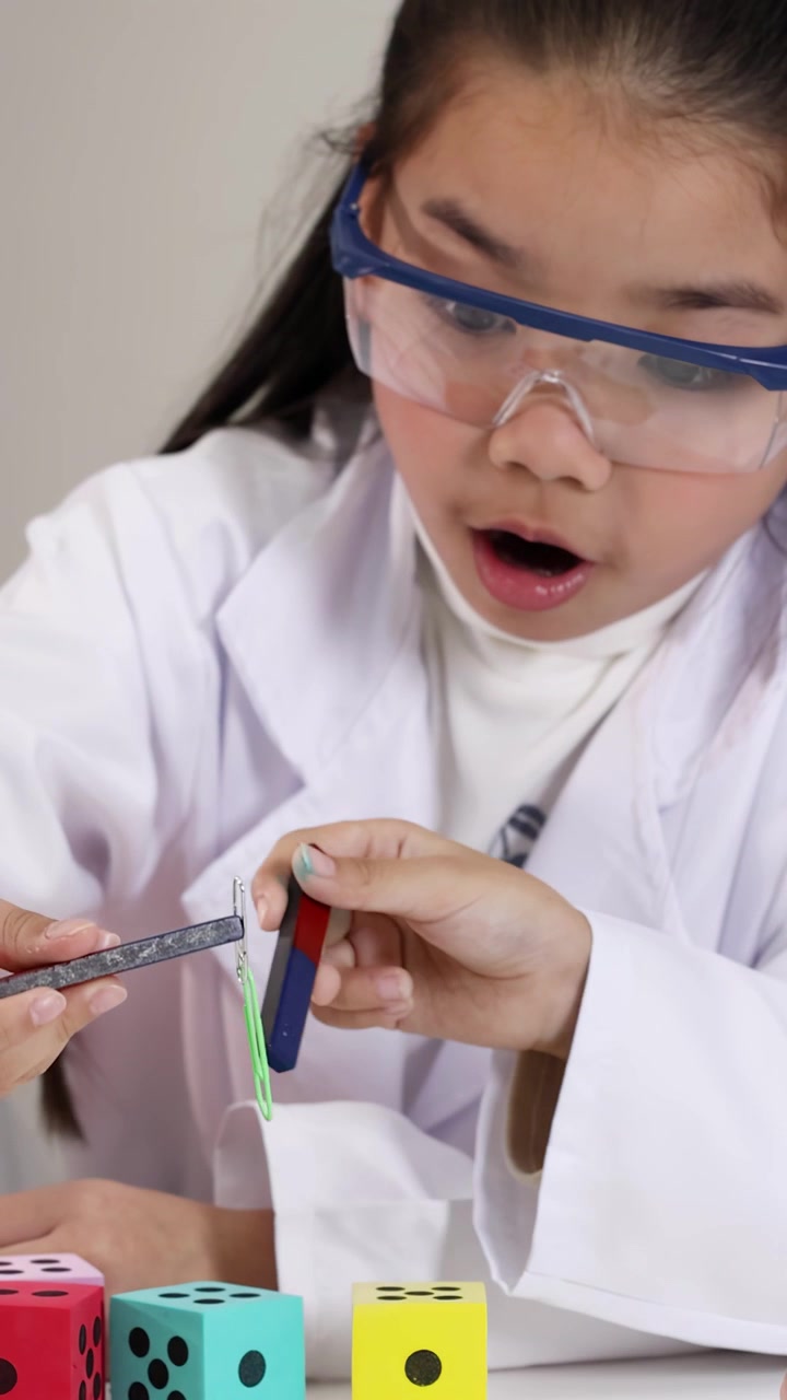 Nuori tyttö laboratoriotakissa tekee tiedekokeita magneeteilla