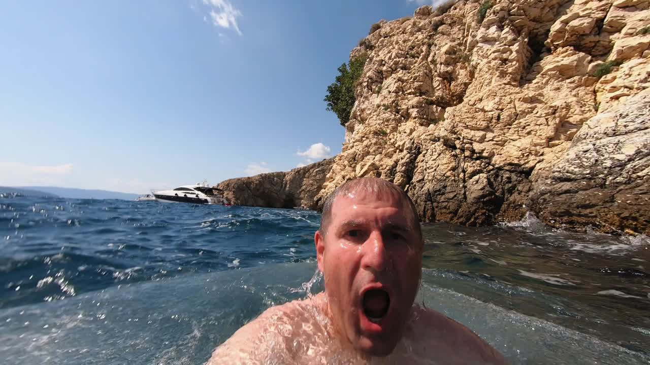 An adult man filming himself while jumping to the sea from a small cliff in Krk, Croatia