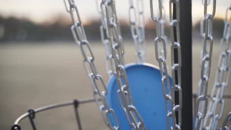 trash panda inner core blue disc golf disc going into black disc golf basket | close up slow motion