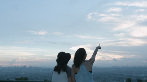 Zwei-Mädchen-Im-Teenageralter,-Die-Ein-Foto-Machen-Und-Auf-Einem-Dach-Auf-Den-Himmel-Der-Stadt-Zeigen