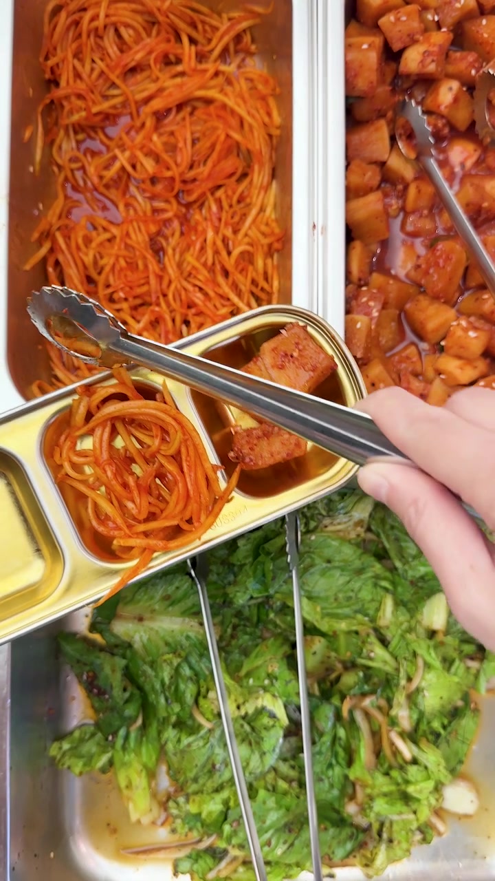 ビュッフェでトングを使って辛い大根と麺のキムチを取り分ける人を上から見た図。