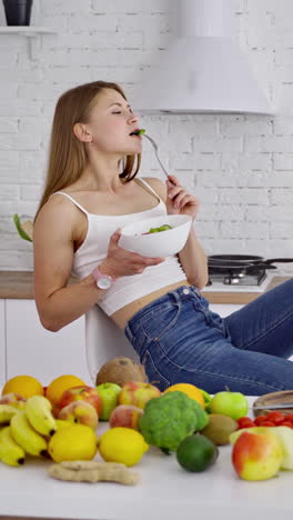 beautiful woman in the light kitchen. young female vegetarian enjoys eating fresh food. organic fruit and vegetables laying on the table. dieting concept. vertical video