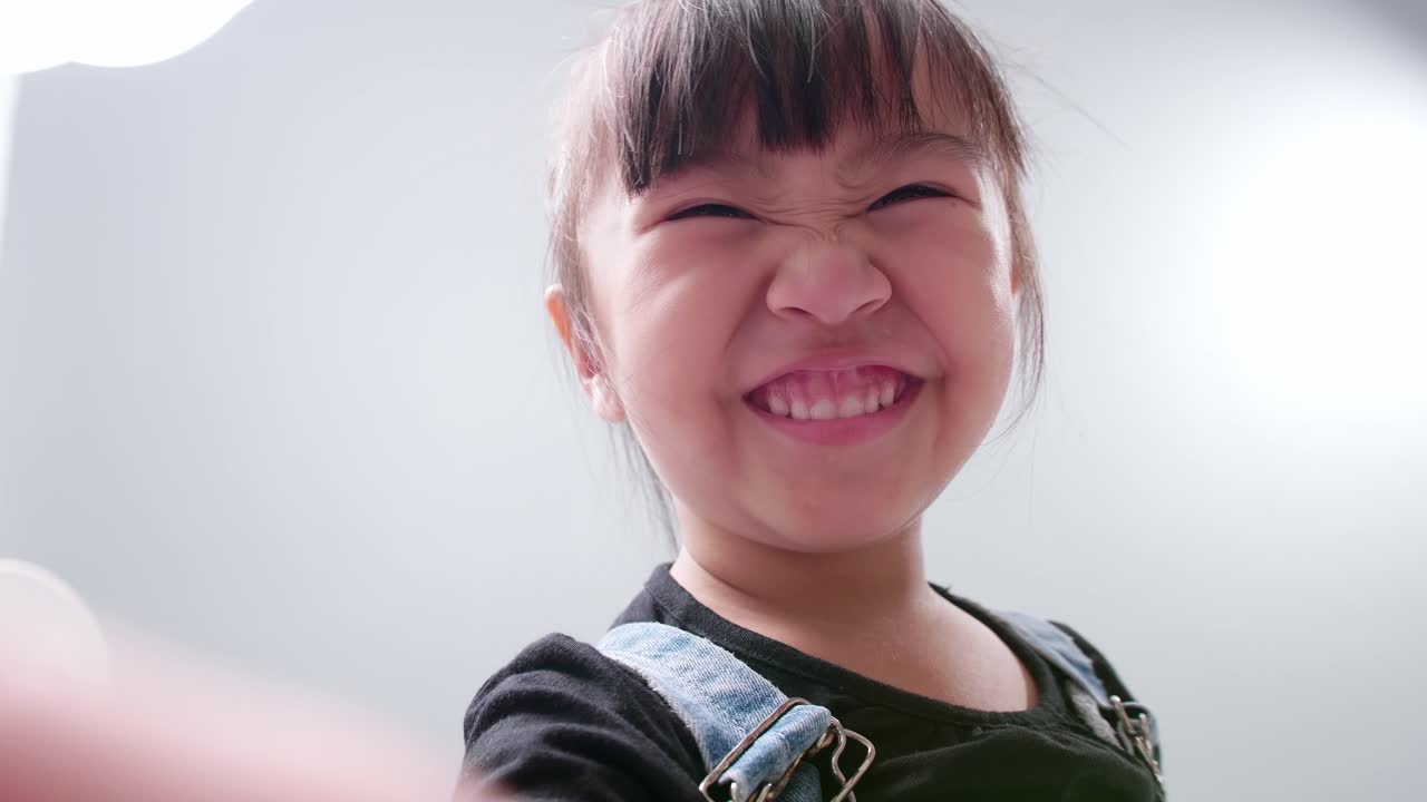 niña asiática feliz usando un teléfono inteligente para videollamadas, saludando con la mano y hablando y hablando con una sonrisa saludando al maestro y a los compañeros de clase
