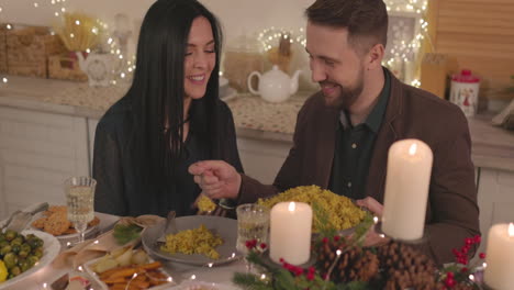 smiling man sitting at table and putting rice in his girlfriend's plate during christmas dinner