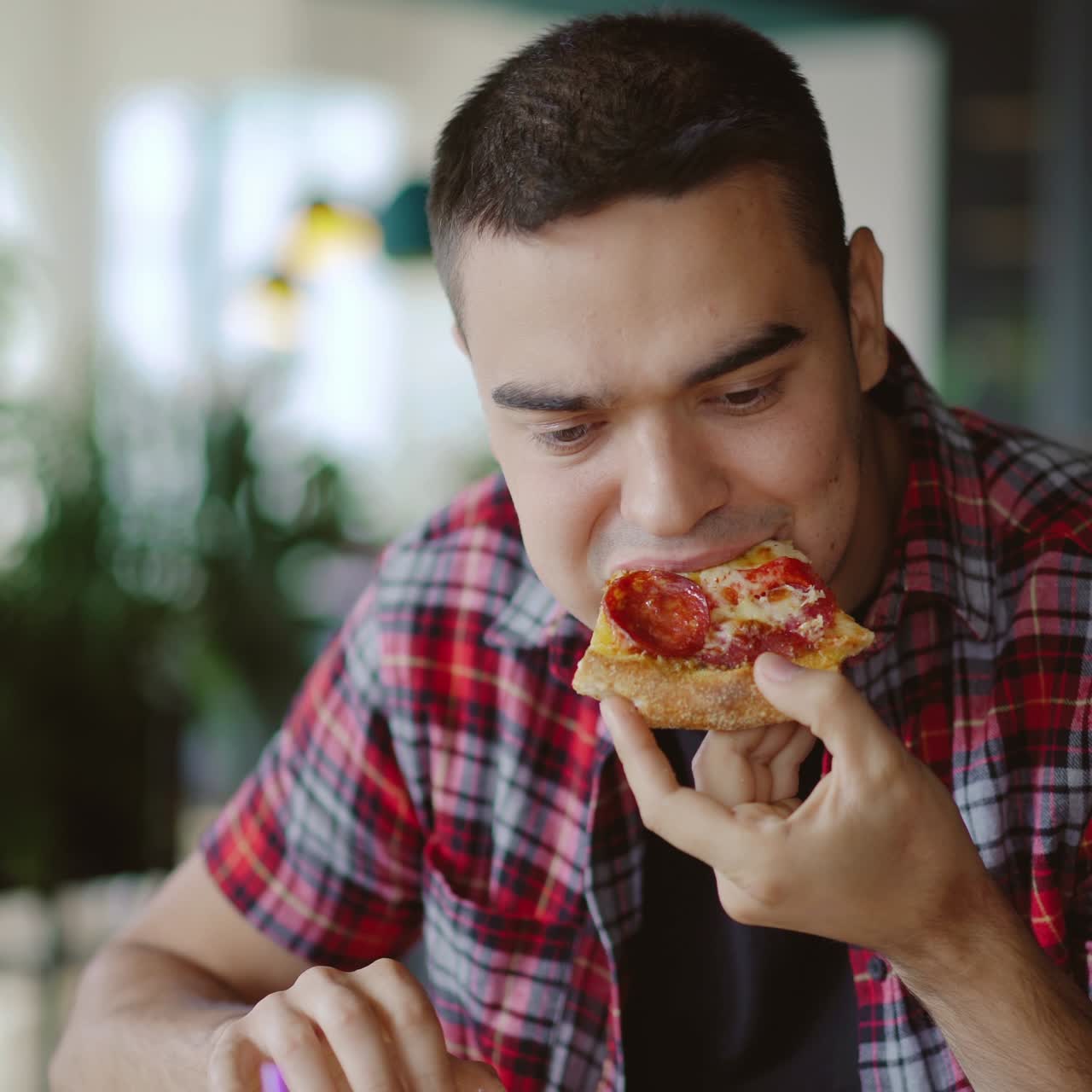 a man in a plaid shirt is eating delicious pizza at a pizzeria in the afternoon