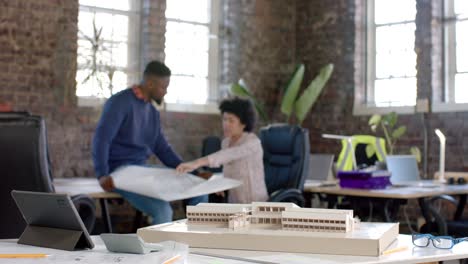 diverse architect colleagues discussing work with building model and blueprint in slow motion