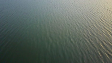 fast-moving low-altitude aerial footage capturing the textured water surface of a lake in uganda, with fine ripples and gradient tones under soft natural light in a minimalist composition