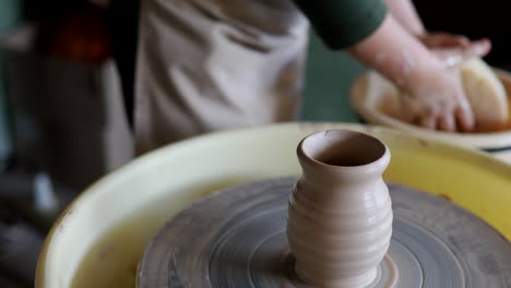 potter child washes his hands against background of rotating jug on pottery wheel.