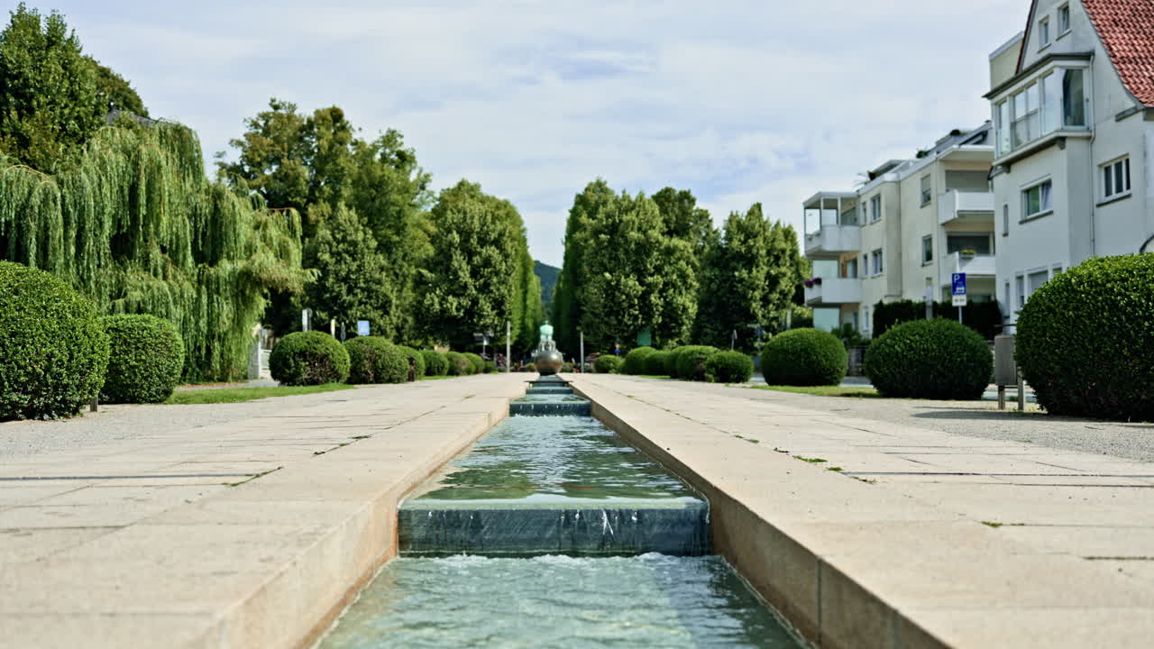 Una plaza peatonal con un río artificial en el centro. Un estanque transitable con bordes de hormigón. Un diseño arquitectónico con un río artificial en un parque urbano.