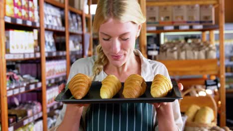 personal femenino sonriente sosteniendo bandeja de croissants en el supermercado
