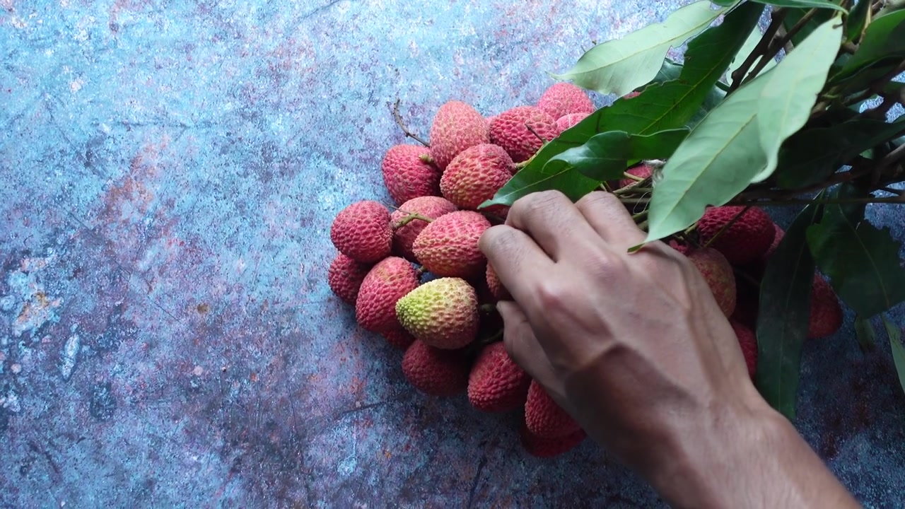 Tangan Menyentuh Buah Leci Segar di Permukaan Bertekstur