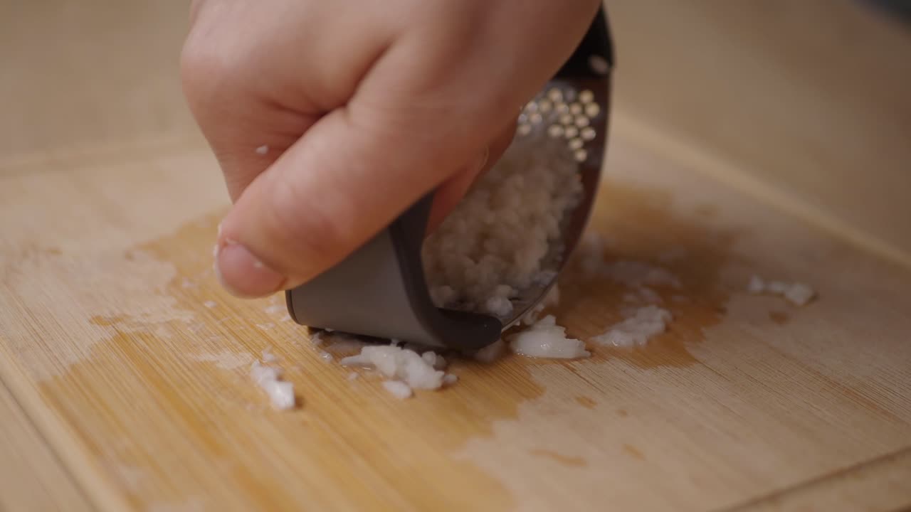 Mano che Schiaccia Aglio su un Tagliere di Legno