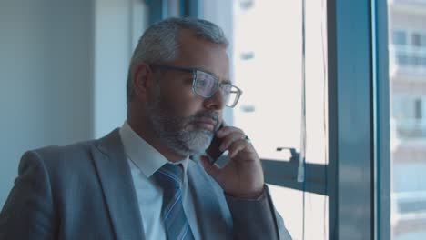 Serious-mature-businessman-standing-near-window