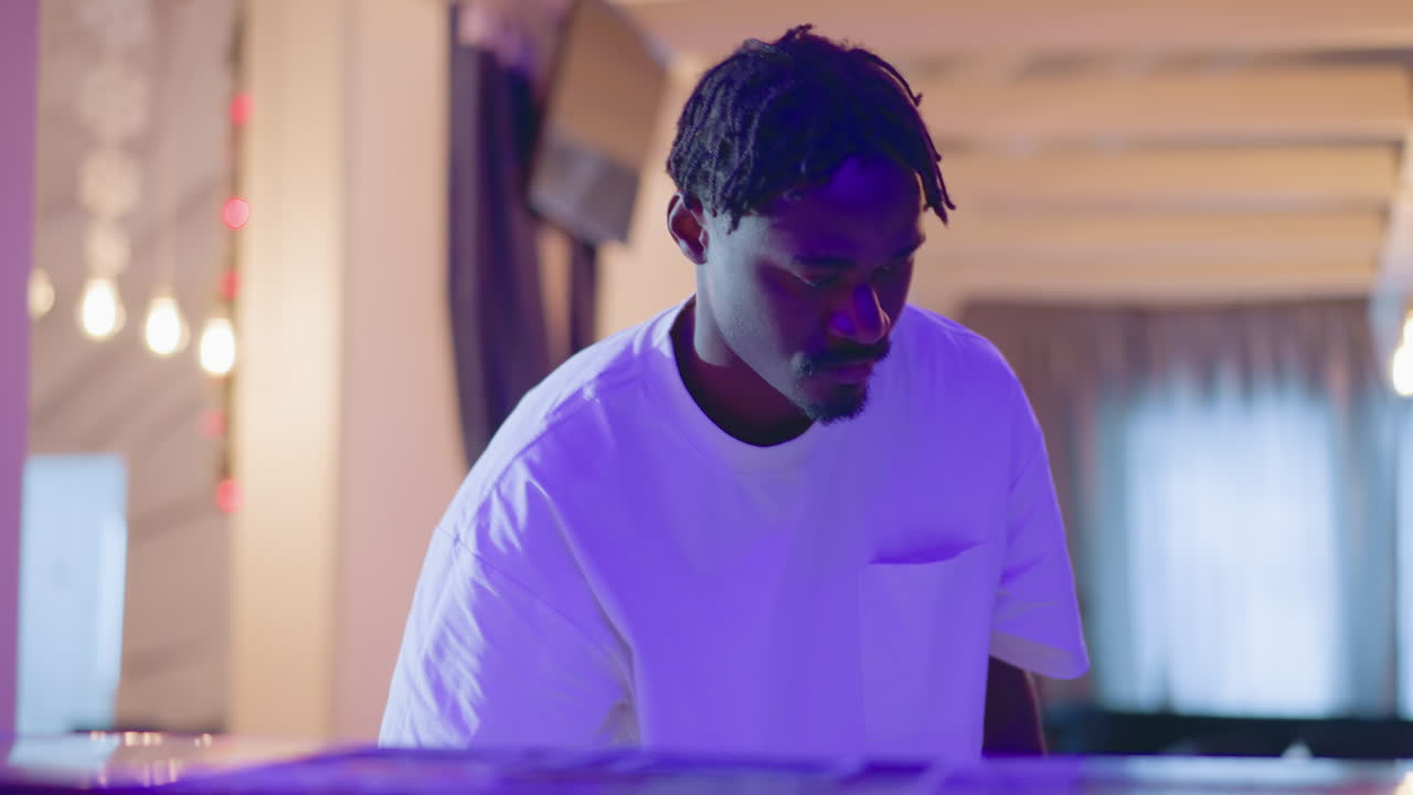 Close-up of a focused man working at bar counter in modern lounge with purple lighting. He is adjusting equipment, preparing for the evening shift in a professional hospitality setting
