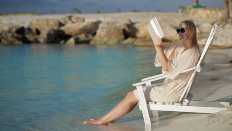 woman with pad making photos of sea sitting in the deck chair on beach