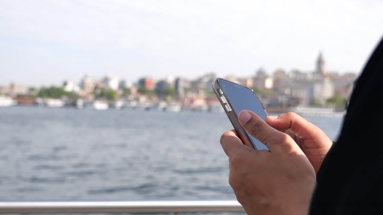 Person holding a smartphone with a city and water in the background