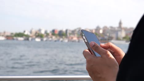 person holding a smartphone with a city and water in the background