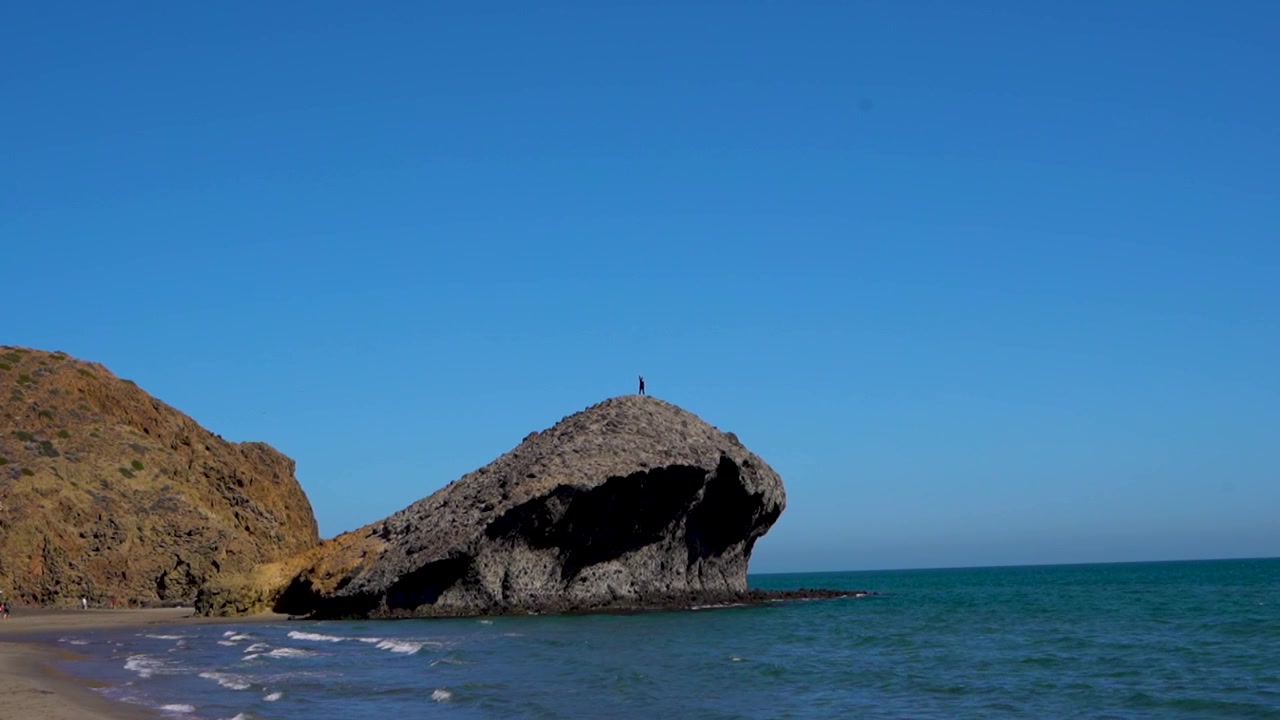 Persona in posa in cima a una roccia sul mare sotto un cielo azzurro limpido.
