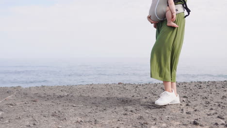 a joyful family walks along the seaside during a sunny summer day. the mother carries her baby in a kangaroo backpack, immersed in nature's embrace