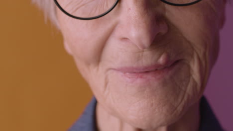 vista de cerca de la mitad de la cara de una anciana rubia con pantalones azul y anteojos, mirando la cámara con lágrimas en los ojos sobre fondo naranja y morado