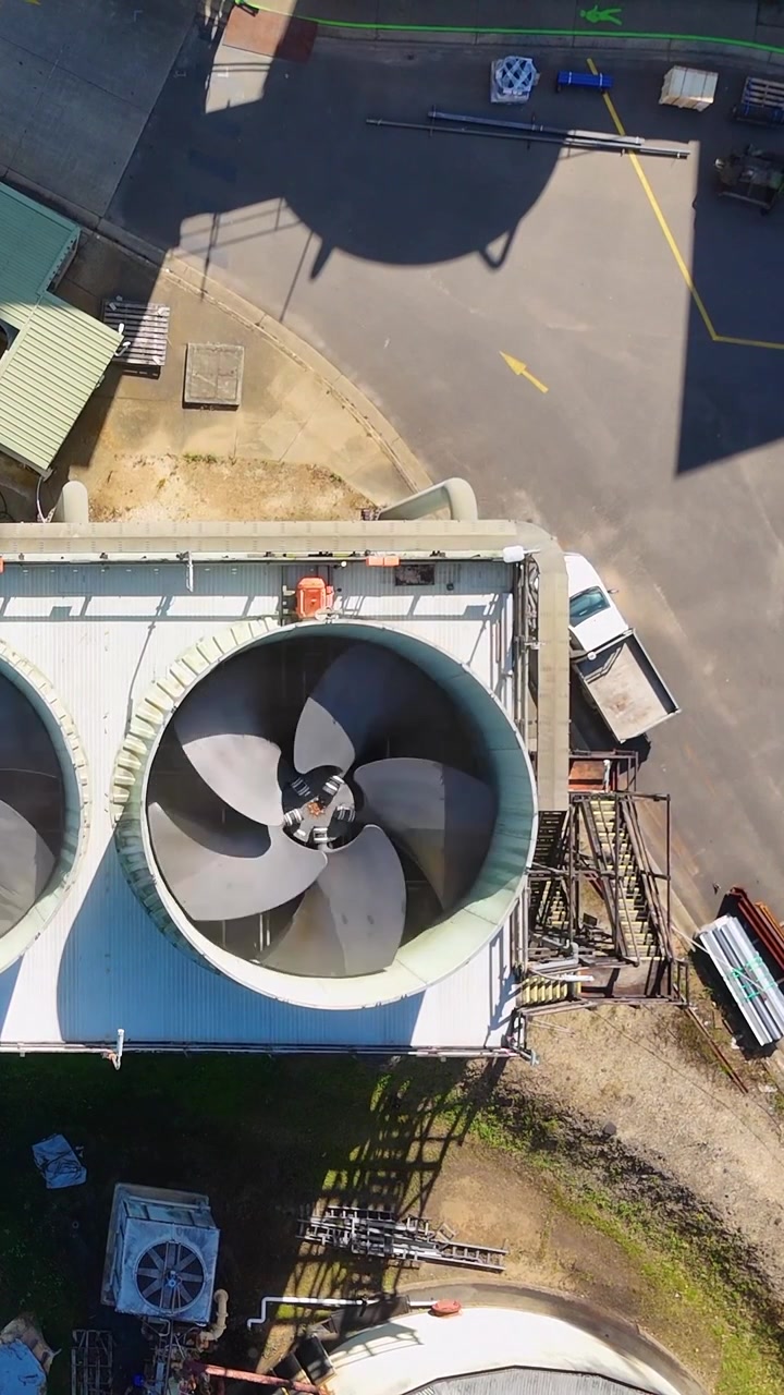 Top-down drone shot of a spinning industrial ventilation fan at a manufacturing facility.