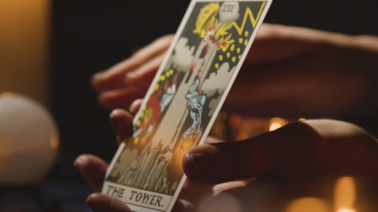 primer plano de una mujer dando lectura de cartas del tarot en una mesa a la luz de las velas sosteniendo la carta de la torre 3