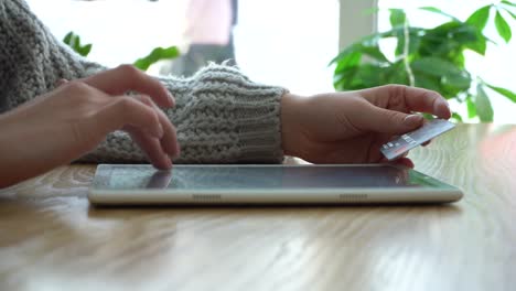una chica está sosteniendo una tarjeta de crédito y usando una computadora tablet mientras está sentada en una cafetería haciendo una compra