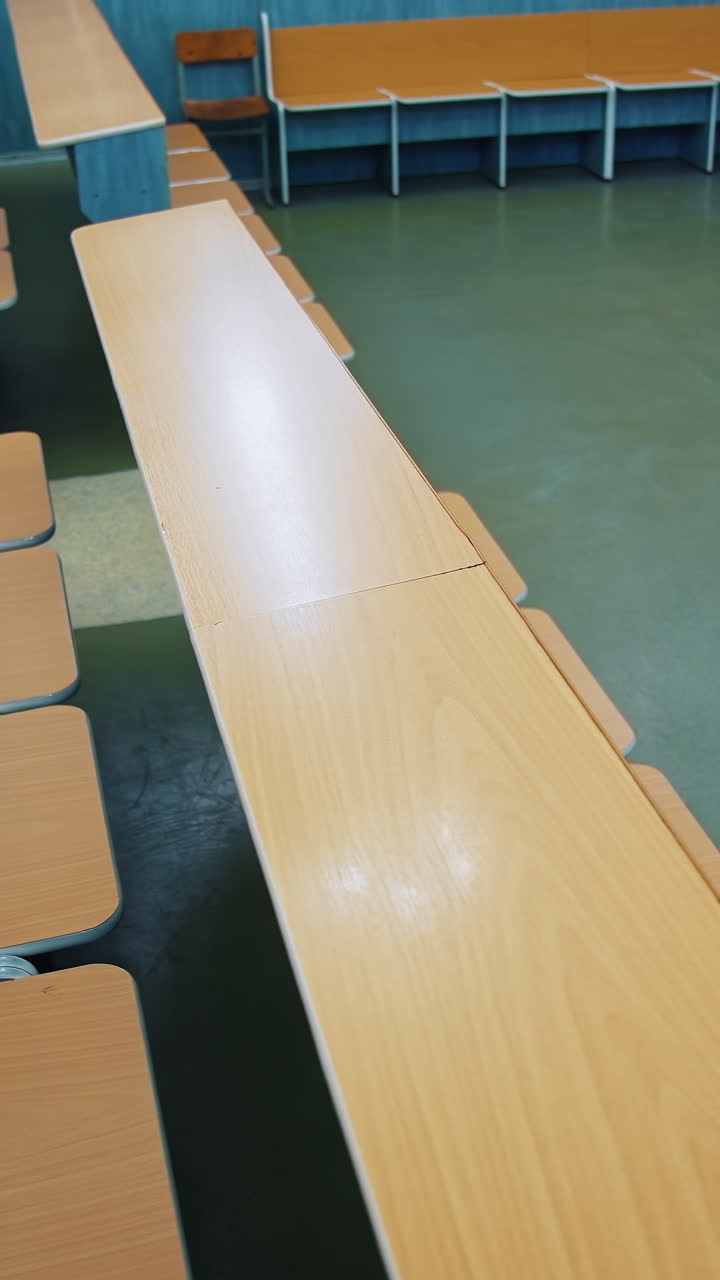Empty auditorium for students. Rows of wooden tables and chairs in the university. Nobody in the class during pandemic. Vertical video