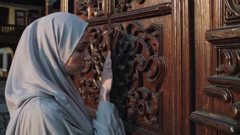 muslim woman touching ornate wooden door, exploring architectural details of historical building, highlighting cultural heritage through delicate interaction