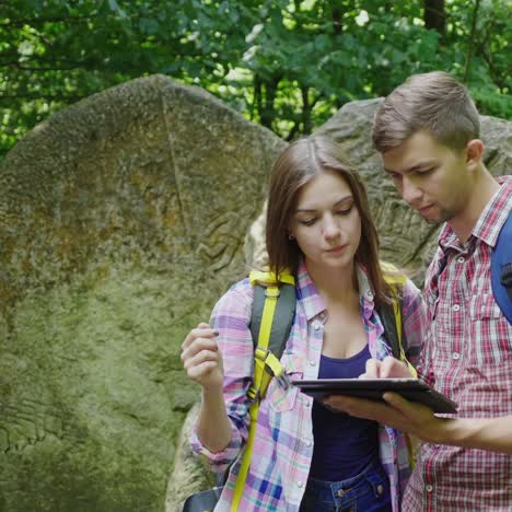 a young couple of tourists with backpacks use a tablet on a trip