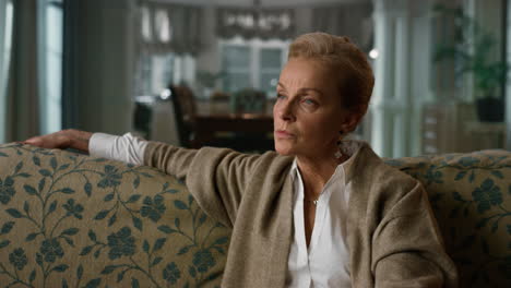 Thoughtful-senior-woman-sitting-on-couch-in-living-room