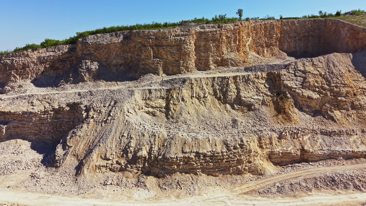 La cantera muestra capas de roca y tierra en una gran área abierta con un camino de tierra que la atraviesa por el medio.