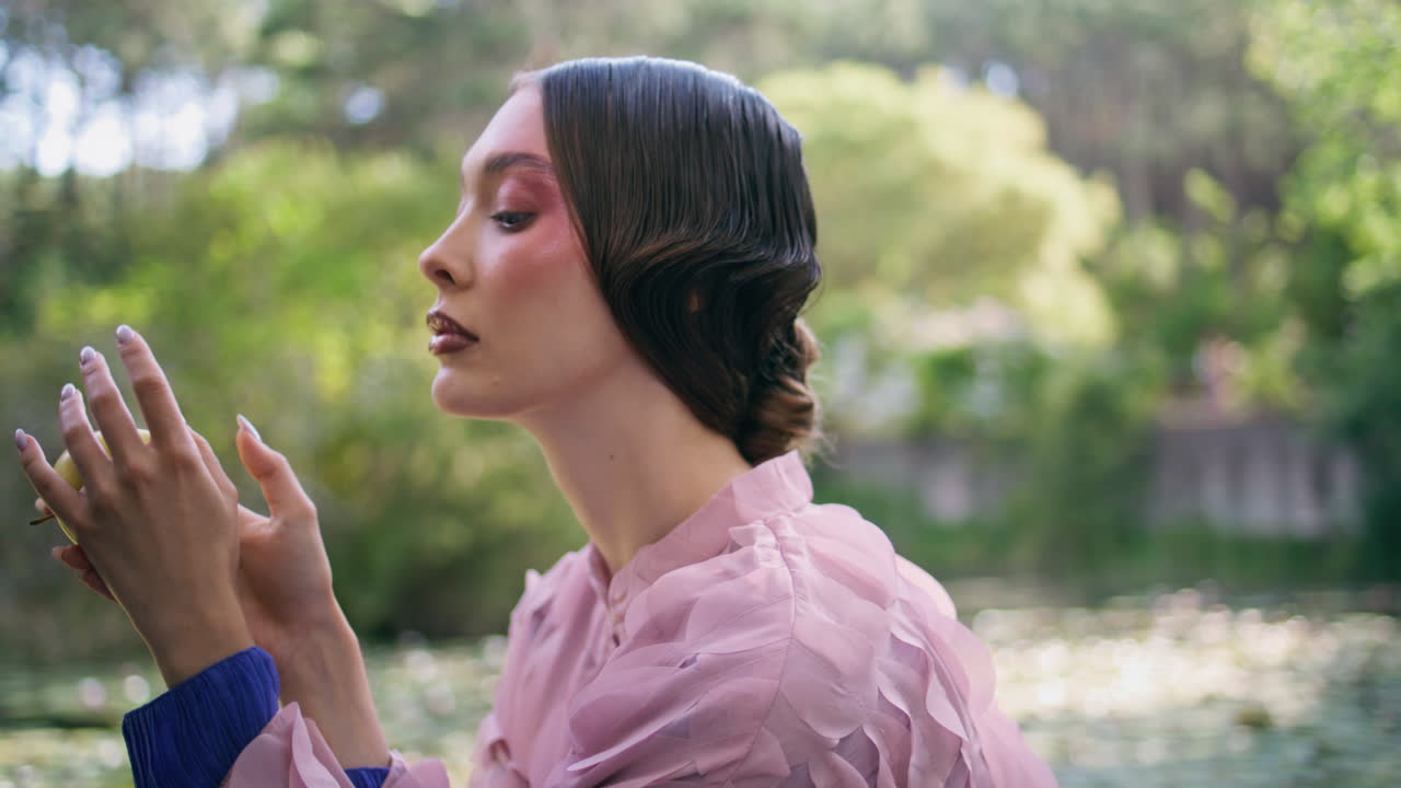 사과를 들고 숲의 연못에 앉아 있는 매력적인 여자. 매혹적인 소녀