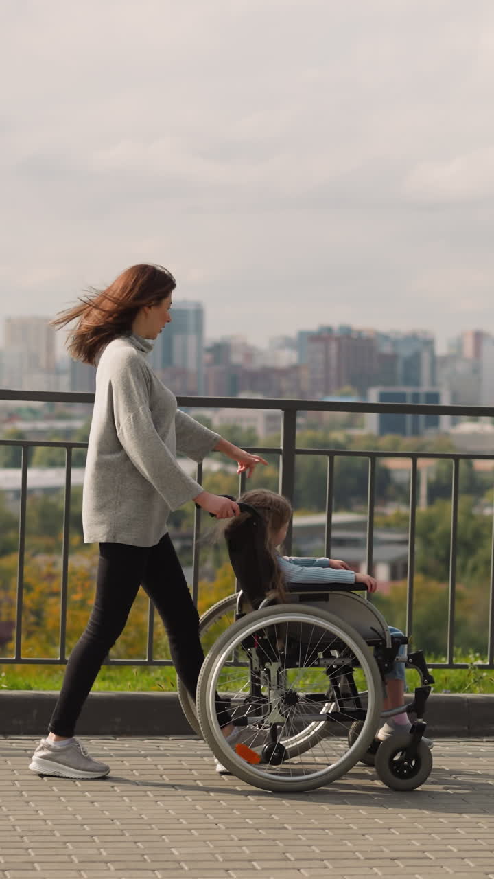 madre muestra panorama de la ciudad a la hija pequeña sentada en silla de ruedas. mujer alegre y niña con parálisis disfrutan de caminar en el parque en un soleado día de primavera